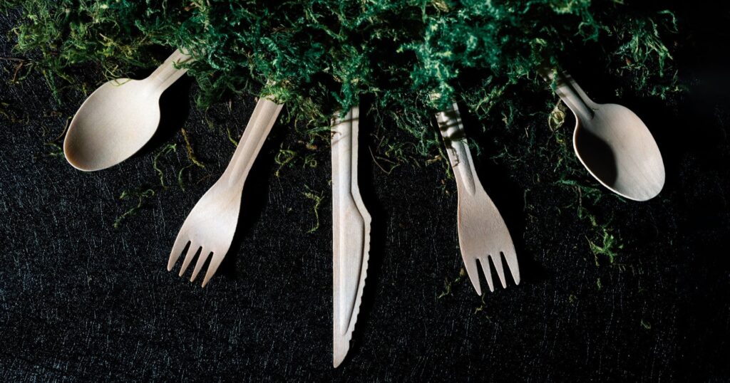 wood cutlery in half circle with green moss on black background