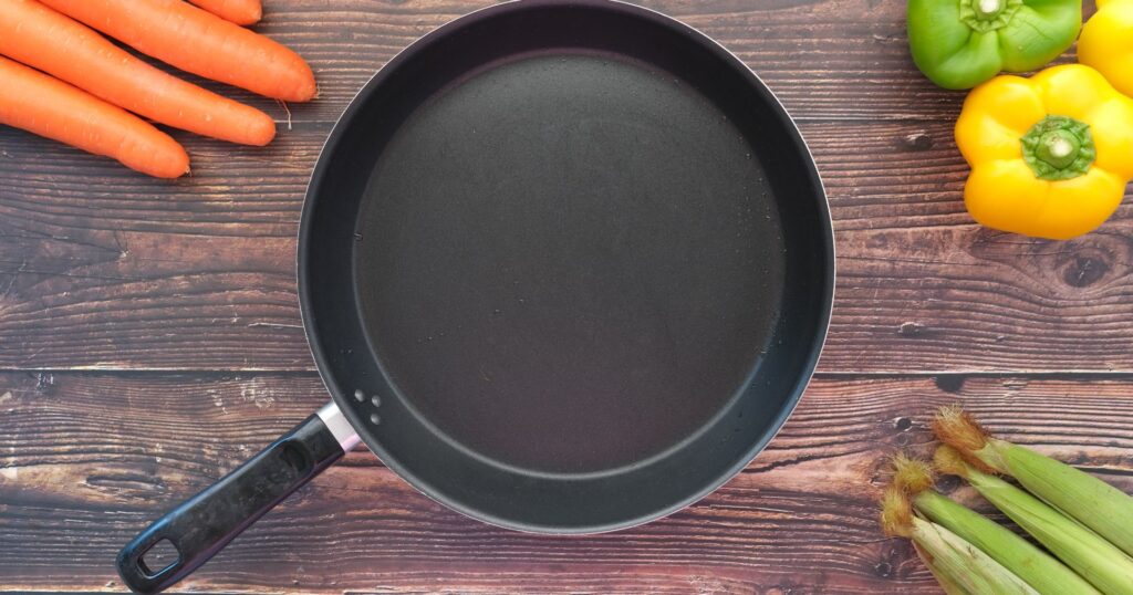 PFAS: non-stick pan on wood table with vegetables surrounding it