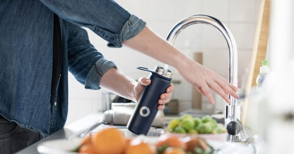 person filling reusable water bottle: earth month ideas