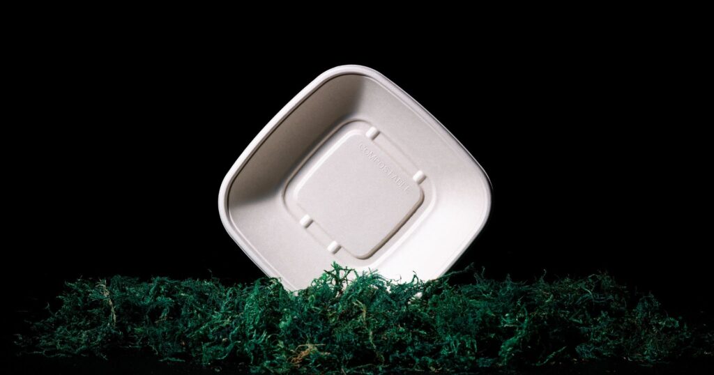 Bagasse compostable takeout container on it's side in moss
