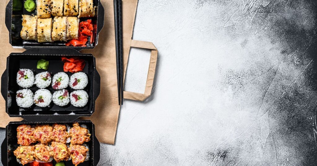 black takeout trays with sushi in them on a grey background, bc single-use plastic ban