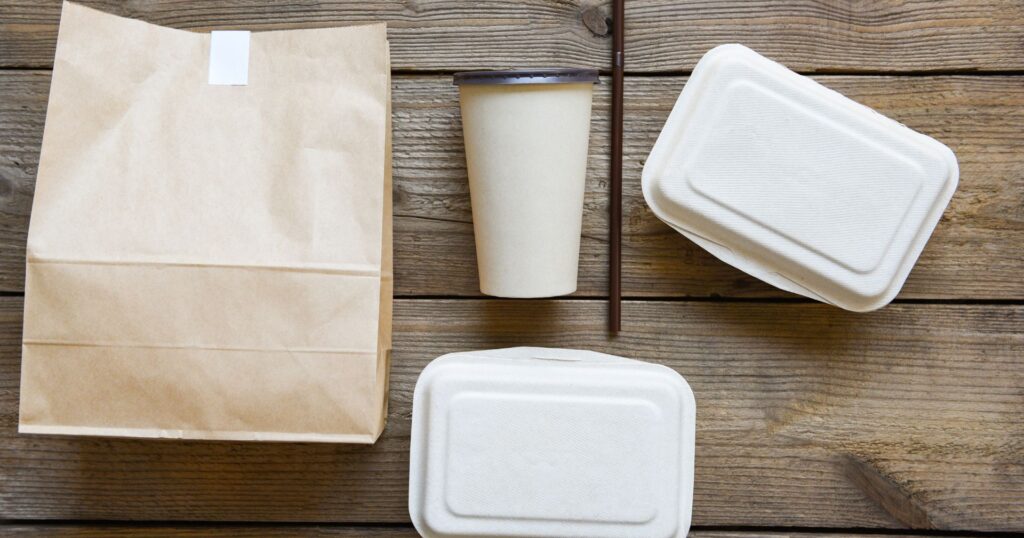 Paper bag, coffee cup, a straw, and two bagasse takeout containers on a wooden table - user experience takeout packaging
