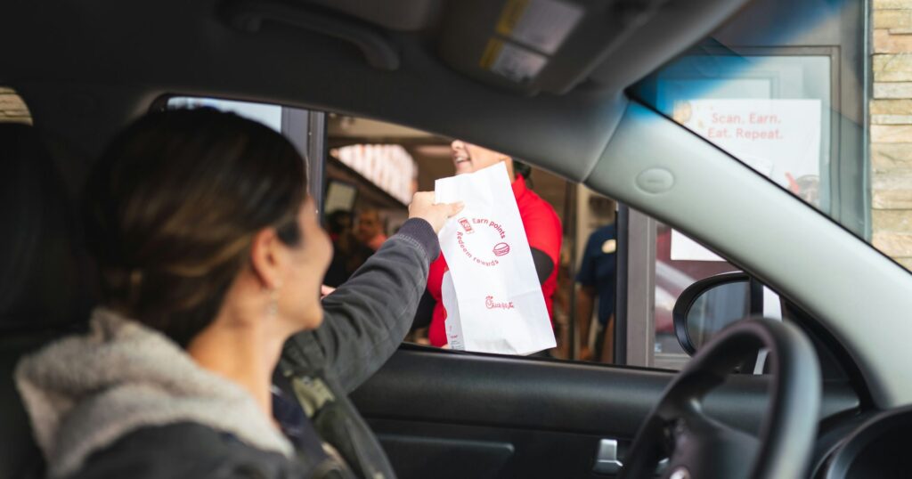 Woman at a drive through reaching for a white paper bag - user experience takeout packaging