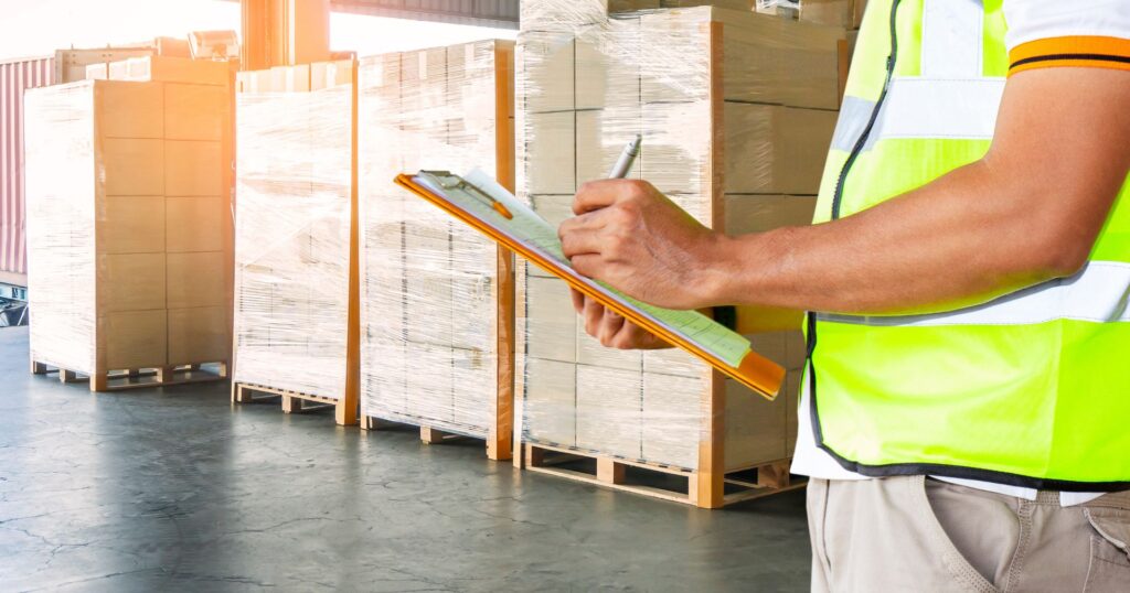 supply chain inventory management, worker checks pallet count on clipboard